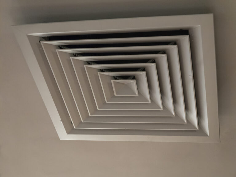 Photo at an angle of a ventilation hatch with a cover with a square pattern hanging on a light ceiling