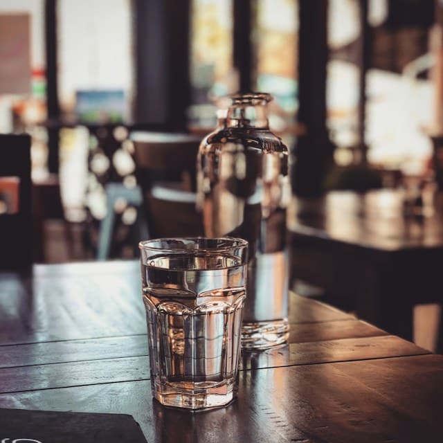 Glass of water with bottle in background